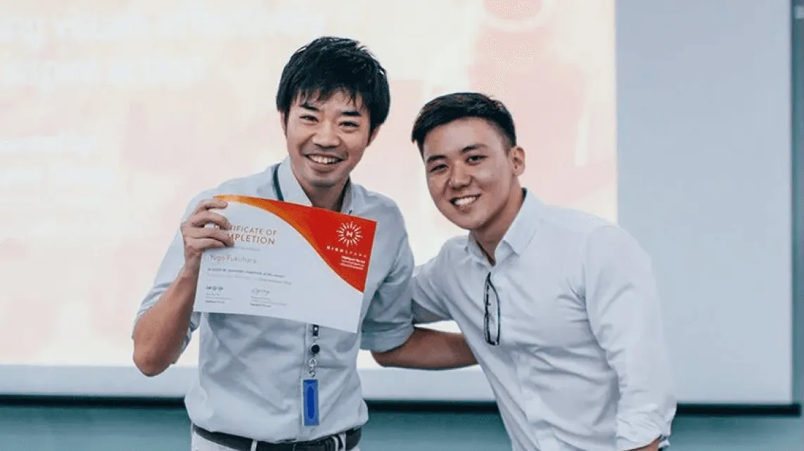 Two smiling men, one holding up a certificate, in front of a presentation screen