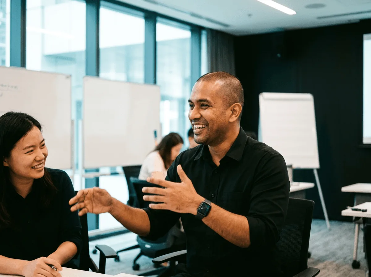 Colleagues laughing and gesturing around a table in a meeting room