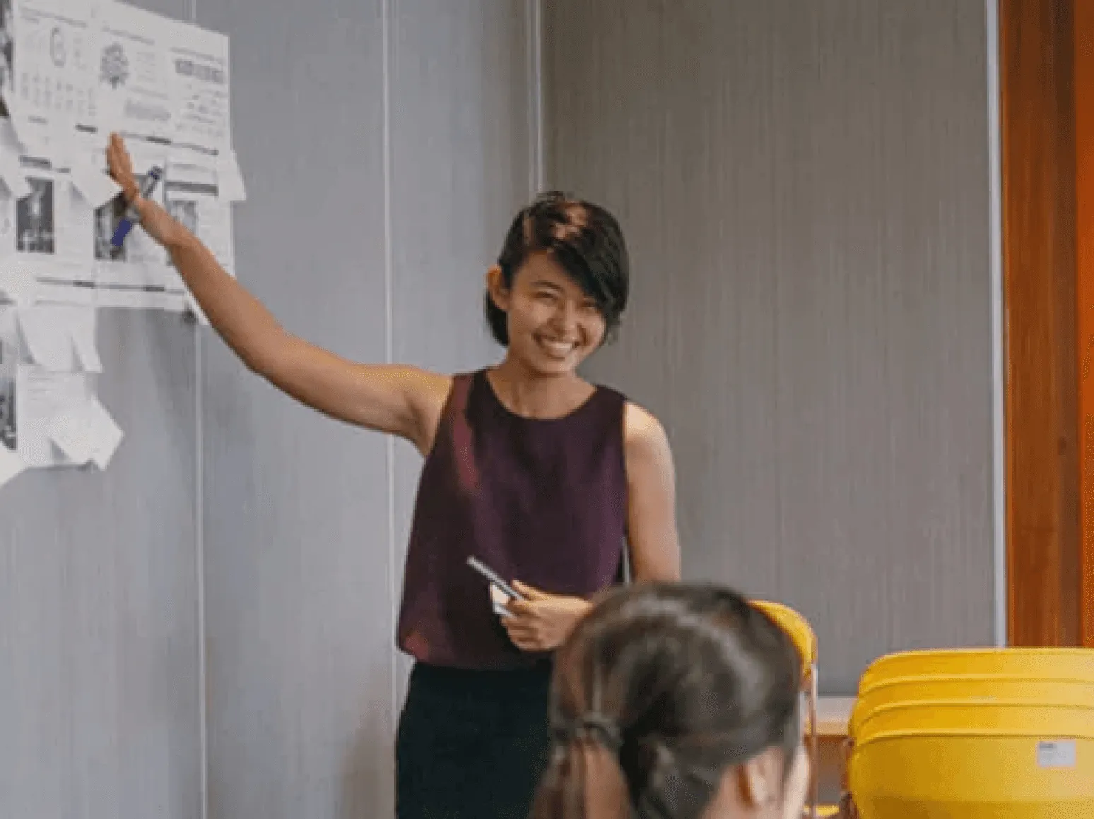 Woman smiling and pointing at a wall of notes during a workshop