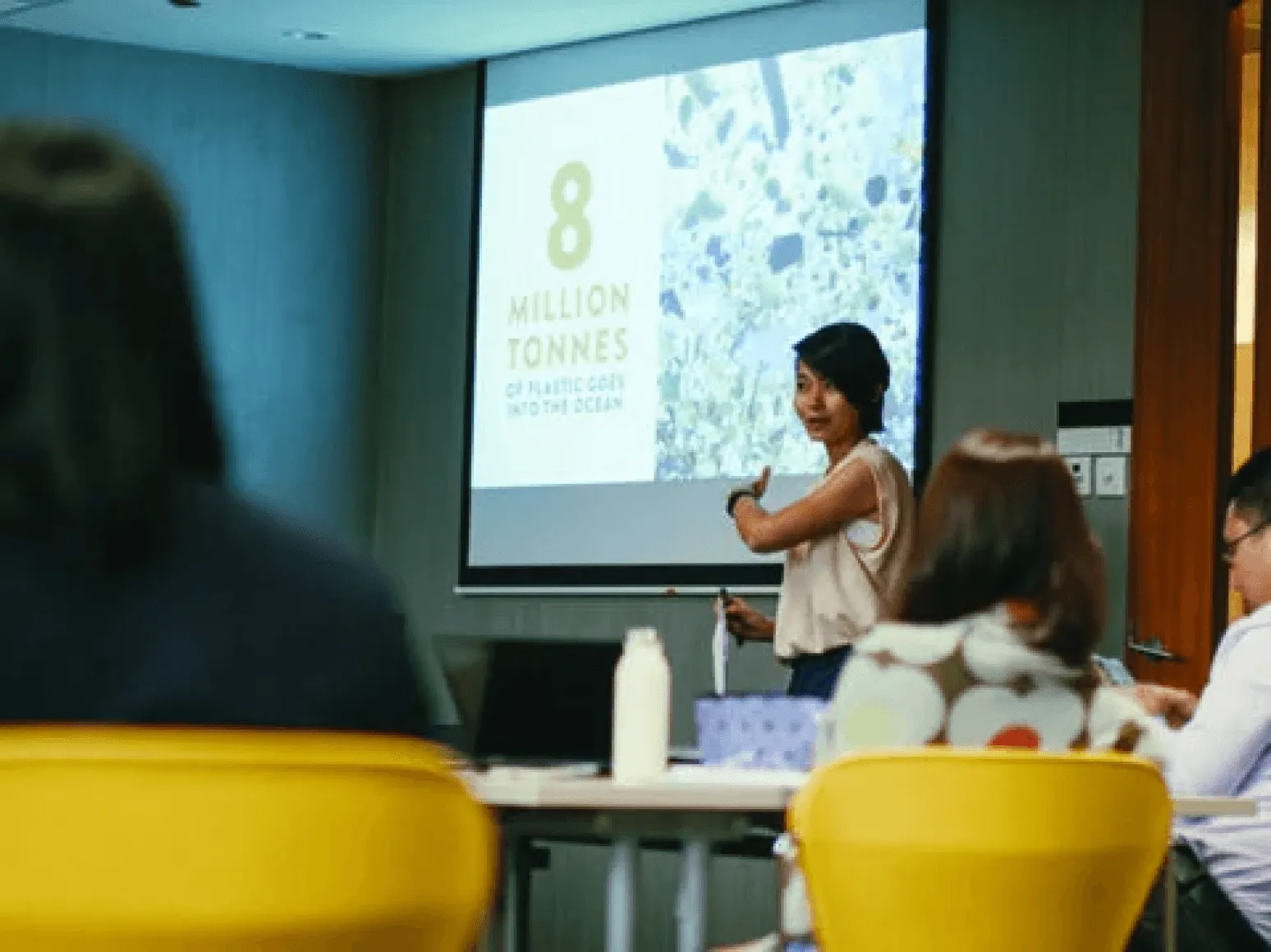 Woman presenting to a class beside a slide that reads 8 million tonnes