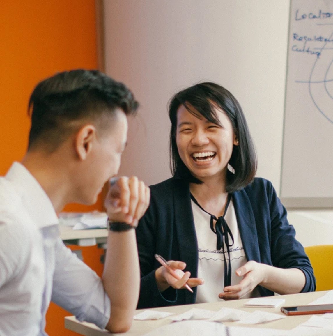 Two colleagues laughing over papers at a workshop table