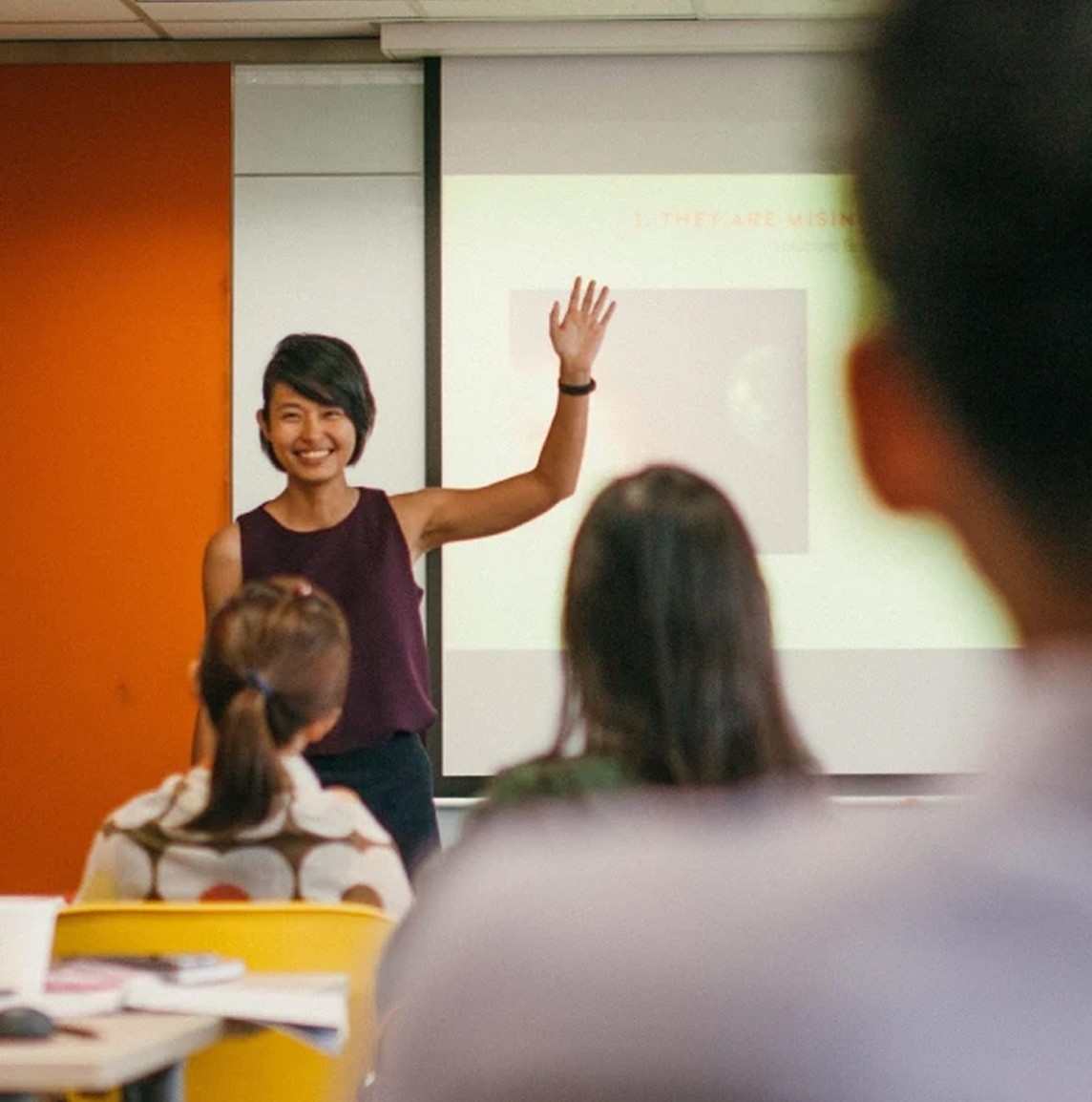 HighSpark trainer gesturing at a projected slide while teaching a seated class